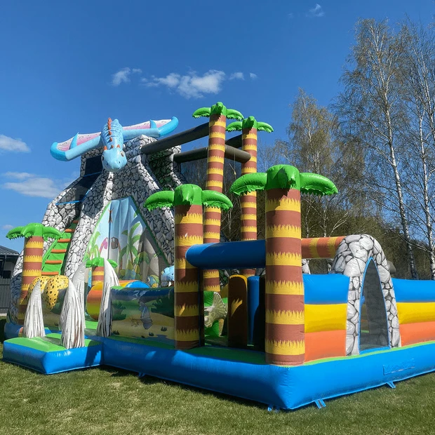 Didelis dinozaurų temos pripučiamas batutas su uolų imitacijos kalnu, palmėmis ir mėlynu pterodaktiliu viršūnėje.